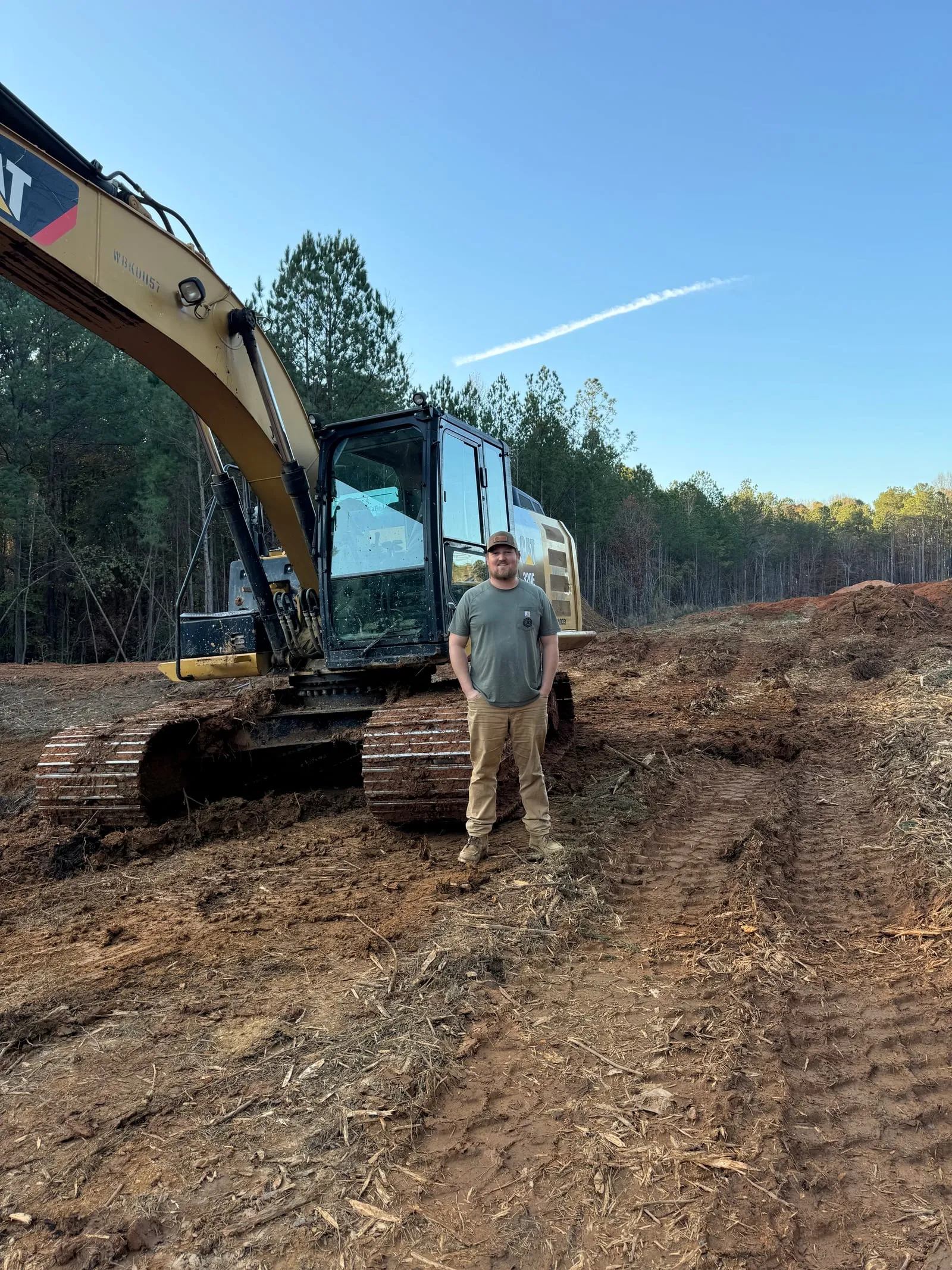 Ballard team member standing in front of a CAT excavator on a freshly cleared site.