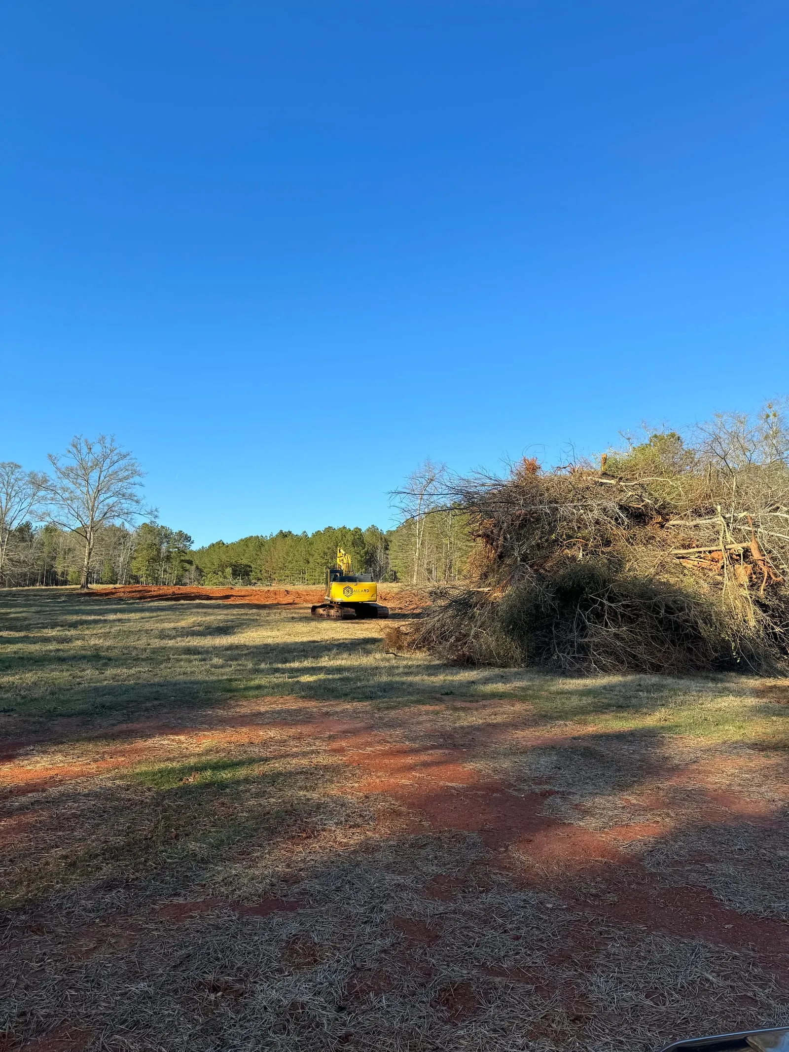 Ballard excavator clearing a field beside a large pile of cleared brush.